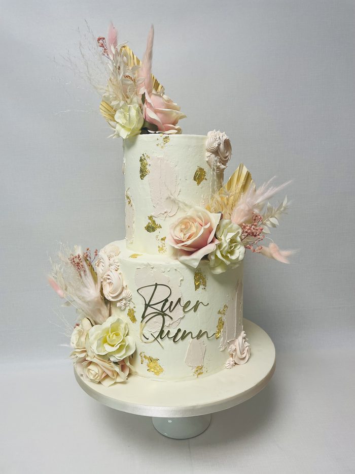 Two tier buttercream christening cake with dried foliage, sugar flowers and a personalised name charm