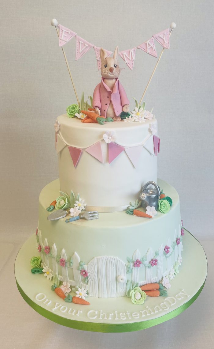 Two tier Beatrix Potter christening cake with a Flopsy Bunny topper, pink bunting and sugar flowers