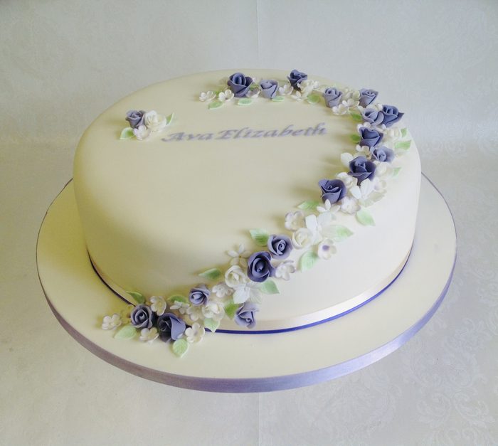 Christening cake with a cascade of purple and white sugar flowers around a piped name