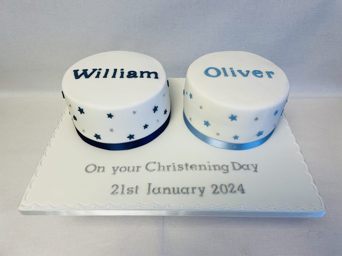 Two small christening cakes side by side for twins, iced with navy stars and William and Oliver name plaques